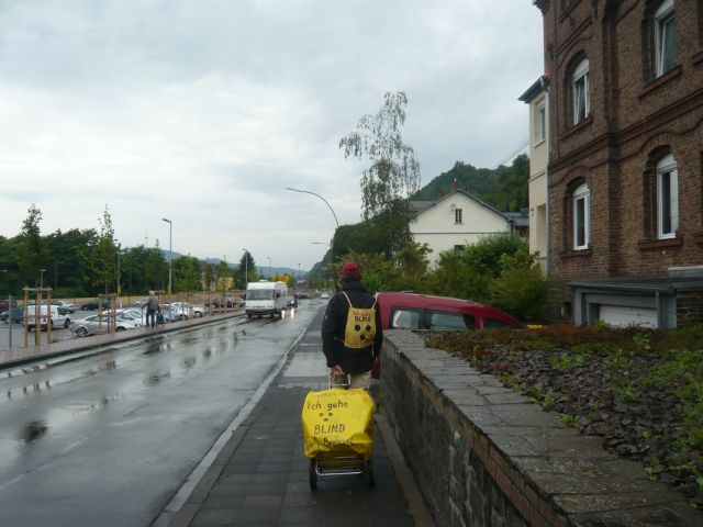 Unterwegs in Braubach am Rhein – mit Langstock und Gepäckanhänger auf dem Weg nach Koblenz Mit Langstock und Gepäcktrolli auf dem Gehweg in Braubach am Rhein bei Regen