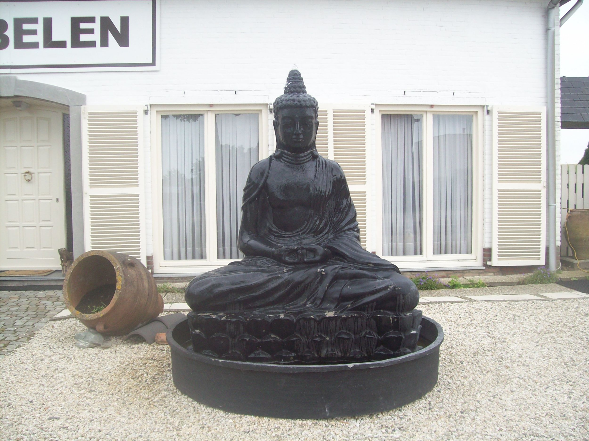 Buddha-Statue als ungewöhnlicher Anblick am Weg nach Tongeren Lebensgroße Buddha-Figur in einem Vorgarten in ländlicher Umgebung